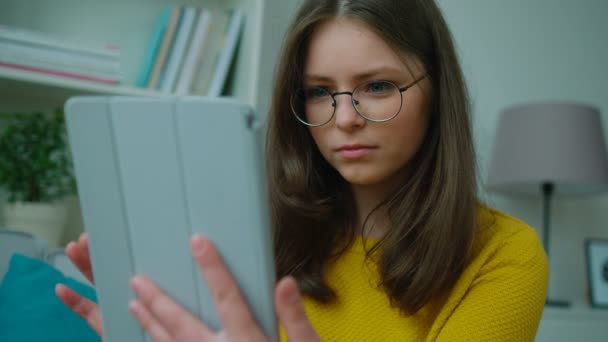 Teenager-Mädchen mit Tablet-Computer, während sie auf dem Sofa im Wohnzimmer sitzt. Mädchen surfen im Internet, sehen Videos und lächeln. Nahaufnahme — Stockvideo