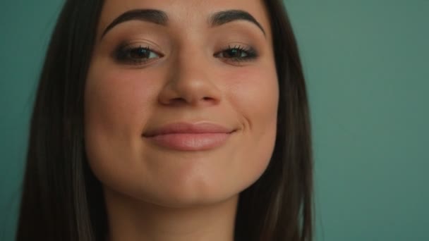 Vonzó fiatal nő mosolyog a kamerába. Közelről portré a kék háttér — Stock videók