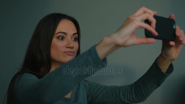 Schöne Frau macht Selfies und posiert drinnen auf blauem Hintergrund. Nahaufnahme — Stockvideo