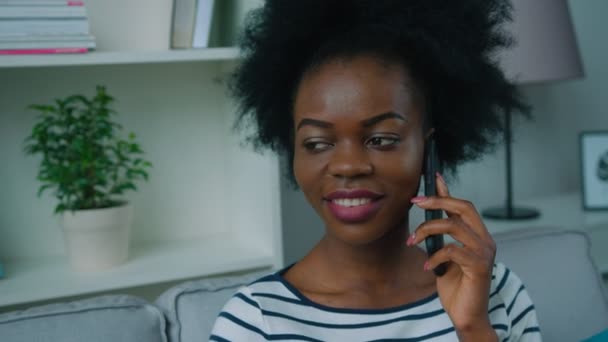 Mujer afroamericana hablando por celular en el sofá de la sala de estar. De cerca. — Vídeos de Stock