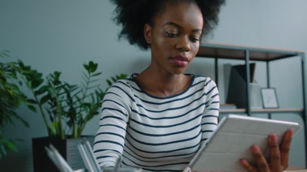 Mujer afroamericana negra usando un dispositivo portátil en la oficina. Mujer sosteniendo la tableta y leyendo. De cerca. — Vídeos de Stock
