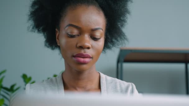 Красивая африканская американка, работающая с ноутбуком в офисе. Женщина думает и улыбается. Портрет крупного плана — стоковое видео