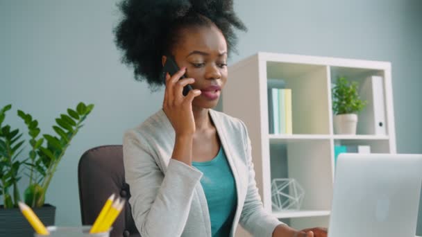 Mujer afroamericana negra hablando por teléfono celular y trabajando con computadora portátil en la oficina — Vídeo de stock