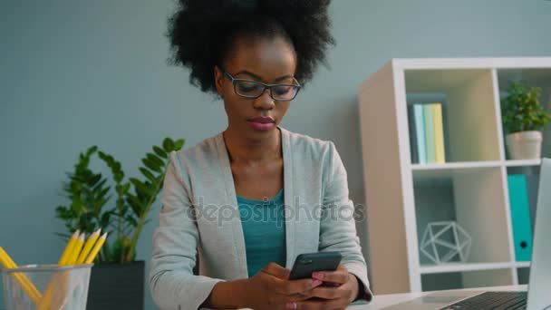 Svart afroamerikanska kvinna bär glasögon och använder smart telefon på kontoret — Stockvideo