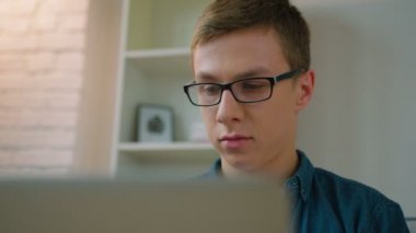 Oturma odasında kanepede oturan ve dizüstü bilgisayar kullanan yakışıklı genç öğrenci. Yakın çekim