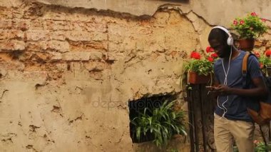 Kulaklık ve cep telefonu şehirde kullanarak müzik dinlemek bardaklarda Afro-Amerikan yakışıklı yan görünüm. Açık.