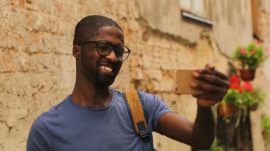 Afro-Amerikan yakışıklı genç gözlük video cep telefonuyla şehir arka plan arkadaş sohbet.