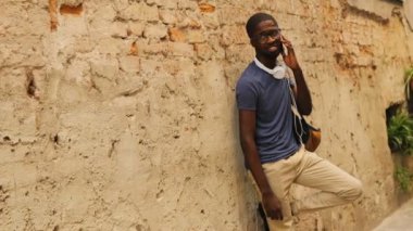 Çekici genç Afro-Amerikan adam gözlük arkadaşıyla şehir duvarının yakınında duran cep telefonuyla konuşuyor. Açık.