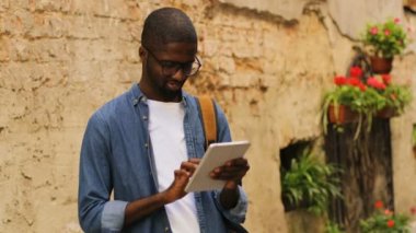 Şehir duvarının yakınında duran arkadaşıyla Sohbet için tablet kullanarak bardaklarda şık genç Afro-Amerikan adam. Açık.