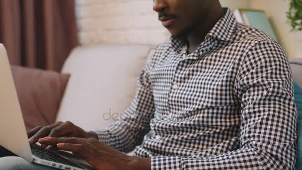 Svart afroamerikanska man använder laptop på soffan i vardagsrummet. — Stockvideo