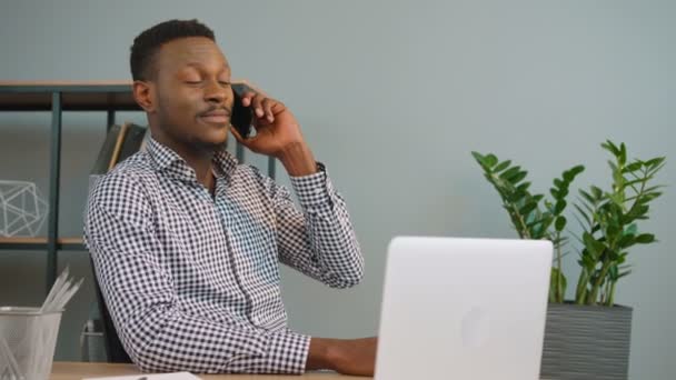 Africano americano homem de negócios falando no telefone celular enquanto trabalhava com computador portátil no escritório — Vídeo de Stock