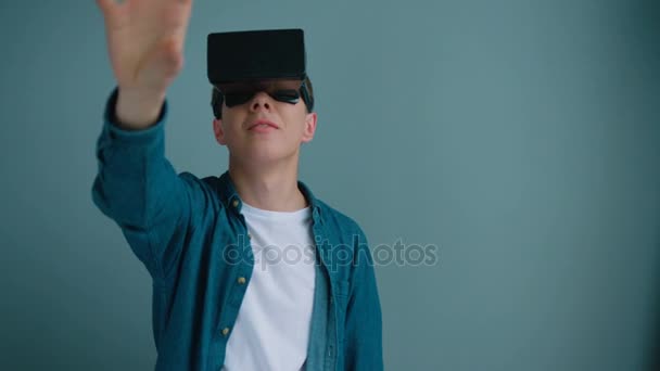 Giovanotto, ragazzo adolescente con occhiali di realtà virtuale su uno sfondo di parete blu. Toccare gli oggetti in cuffia vr — Video Stock