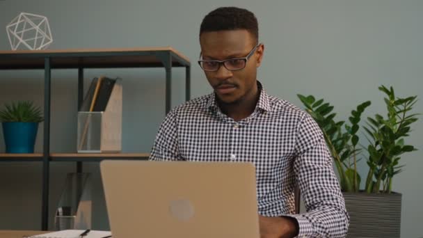 Hombre de negocios afroamericano usando computadora portátil en la oficina. Trabajador de oficina negro mirando el monitor de pantalla y escribiendo algo en el cuaderno . — Vídeo de stock