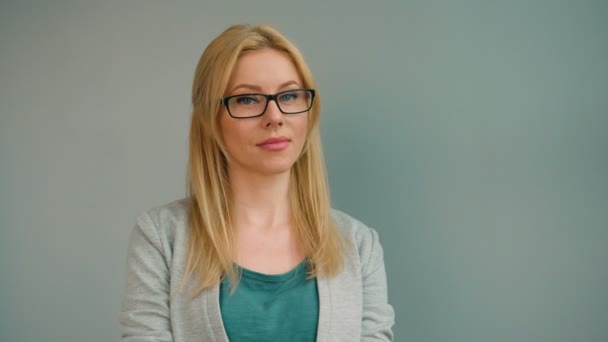 Beautiful blond woman in glasses looking straight at the camera and smiling on grey background. Portrait shot — Stock Video