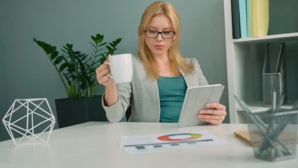 Empresária loira atraente trabalhando com computador tablet e beber café no escritório — Vídeo de Stock