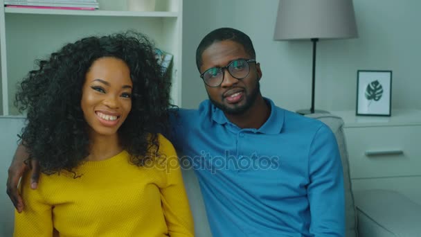 Amantes pareja afroamericana sentados en el sofá juntos, mirando a la cámara y sonriendo. De cerca. — Vídeos de Stock
