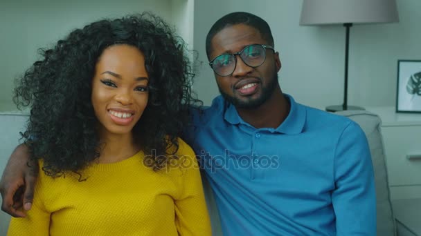 Beautiful african american couple sitting on couch together, looking at the camera and smiling. Close up — Stock Video