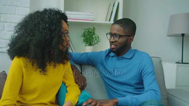 Feliz pareja afroamericana sentada en el sofá juntos, hablando y sonriendo. De cerca. — Vídeo de stock