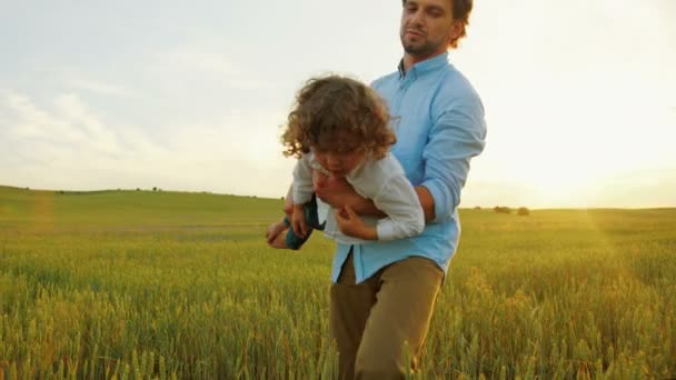 O pai levantou o filho para o céu, fingindo que está a voar. Pai e filho brincando juntos em um campo ao pôr do sol. Fechar — Vídeo de Stock