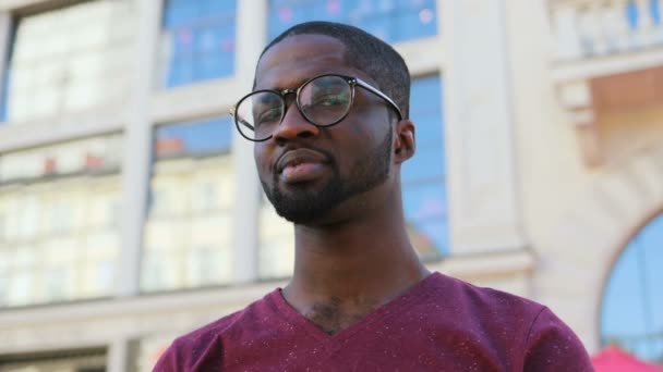 Портрет красенем афроамериканець у келихи, футболка посміхається на фоні міста. Відкритий. — стокове відео