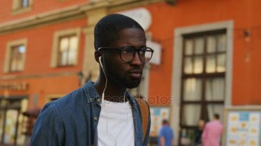 Yakışıklı genç Afro-Amerikan turist bardaklarda şehirde kulaklık kullanarak müzik dinlemek. Açık.