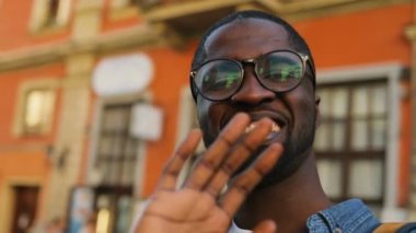 Güzel genç Afro-Amerikan turistik şehir merkezinde akıllı telefon kullanan arkadaş sohbet gözlük video portresi.