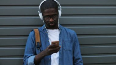 Kulaklık ve akıllı telefon kullanarak müzik şık genç Afro-Amerikan turist. Açık.