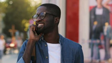 Mavi gömlekli arkadaşım ve şehir merkezinde dişleriyle gülümseyen akıllı telefonda konuşurken şık Afrika turistik portresi. Açık.