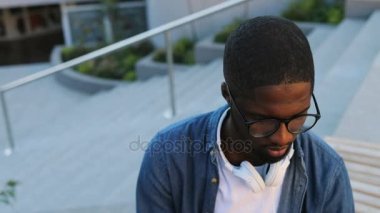 Gözlük ve kamera için arka plan üzerinde merdiven ile seyir kulaklık ile genç Afrika adam portresi. Açık.