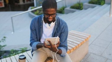 Çekici Afrika adam gözlük ve tablet kullanma ve içme kahve merdiven zemin üzerine bankta otururken kulaklık.