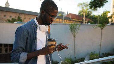 Cep telefonuyla kulaklıklarla bardaklarda iyi Afrika genç adam yıldız şehir arka plan üzerinde giderken kahve içme.