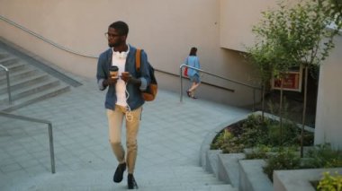 Genç Afrika adam akıllı telefon kullanarak ve şehir yıldızlarda giderken kahve elinde tutan kulaklıklarla bardaklarda.