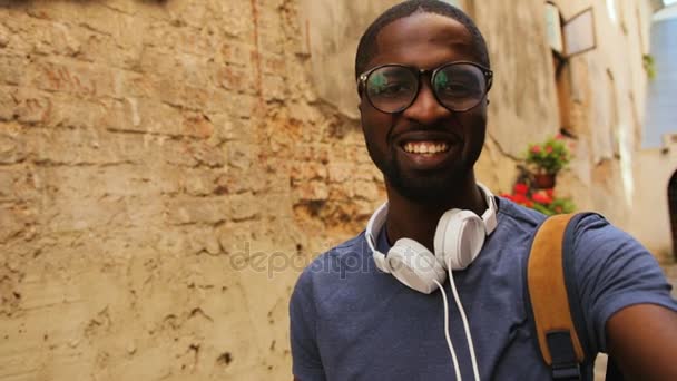 Aantrekkelijke jonge Afro-Amerikaanse man in glazen videochat op slimme telefoon met je vriend op zoek naar camera in de stad. Buiten. — Stockvideo