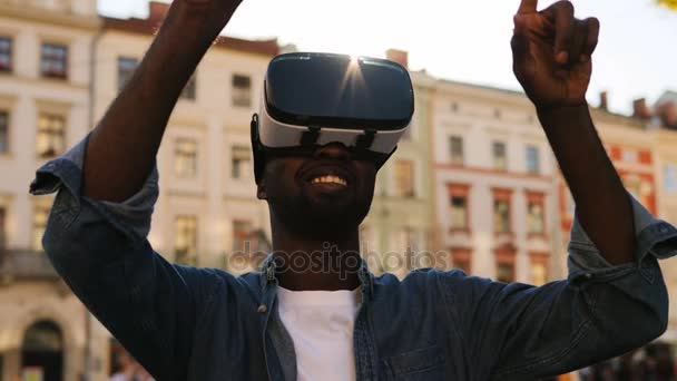 青いシャツを着て市内中心に立って、ビデオゲームのためのデバイスを使用して魅力的なアフリカ系アメリカ人の肖像画. — ストック動画