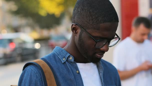 Retrato de turista africano atraente com óculos em camisa azul posando para a câmera, sorrindo com os dentes de pé no centro da cidade . — Vídeo de Stock