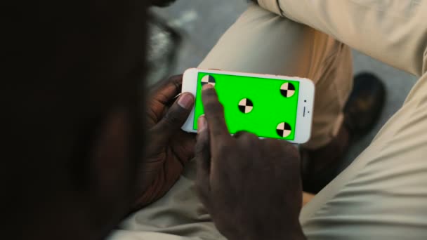 Vue arrière de l'homme afro-américain utilisant un téléphone portable blanc avec écran vert de mouvement de piste. Extérieur . — Video