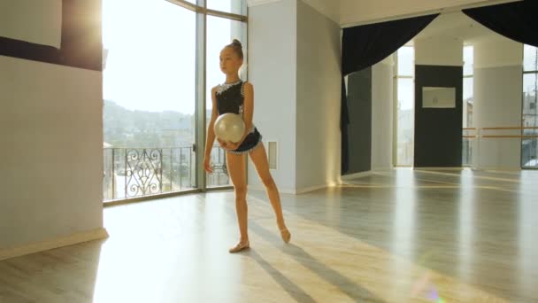 Jeune fille s'entraînant à l'exercice de gymnastique avec une balle dans le studio de ballet sur fond de soleil . — Video