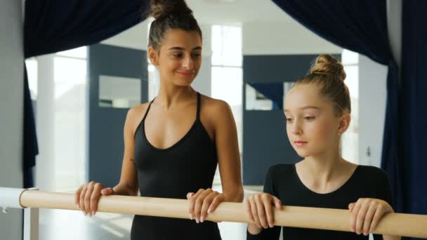 Zbliżenie portret młodej nauczycielki tańca i jej uczennicy patrzących na siebie i uśmiechających się do kamery w studiu baletowym. — Wideo stockowe