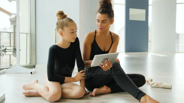 Junges Mädchen und ihr Lehrer beobachten etwas auf dem Tablet, während sie sich im Studio entspannen. — Stockvideo