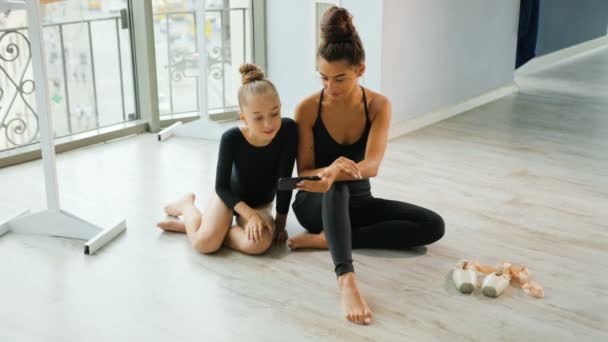 Jeune fille et son professeur regarder quelque chose sur le téléphone intelligent tout en se relaxant dans le studio . — Video