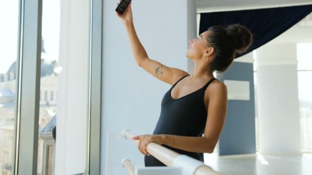 Retrato de bailarina atraente em pé perto do ballet barre e fazer selfie no telefone inteligente . — Vídeo de Stock