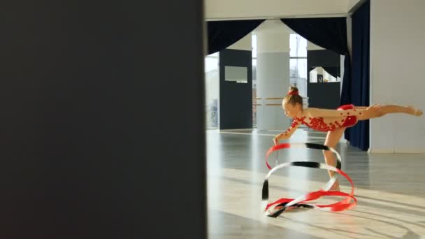 Liten flicka i röd kropp gör gymnastik utövandet och spinning menyfliksområdet i eleganta studio och possing till kameran — Stockvideo