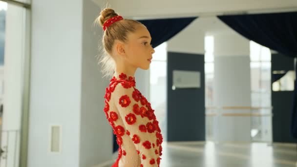 Side portrait of little graceful gymnastics spinning the red ribbon in front of camera in the white studio. — Stock Video