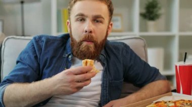 Oturma odasında evde tv izlerken pizza yemek sakallı çekici adam portresi. Yakın çekim.