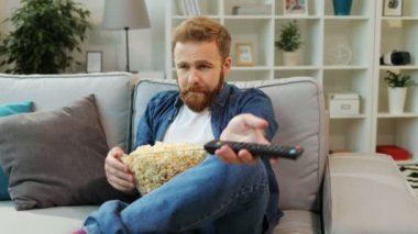Patlamış mısır yemek ve kanepe oturma odasında otururken ilginç Filmler TV arama genç seriuos adam.