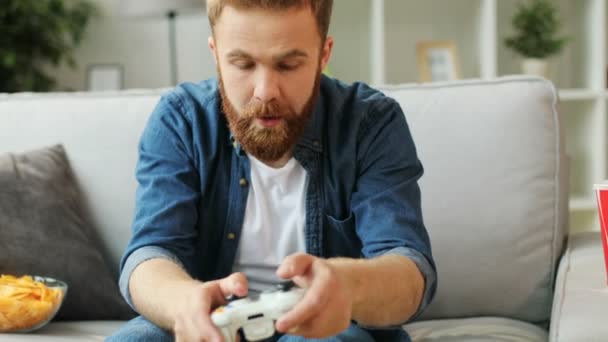 Emocionální mladíka v ležérní tričko hrát hru na xbox, zatímco sedí na gauči doma v obývacím pokoji. Muž, relaxaci při hraní her.