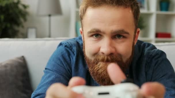 Retrato del hombre emocional con barba jugando videojuego en xbox y tratando de ganar mientras está sentado en el sofá en casa en la sala de estar. De cerca. . — Vídeo de stock