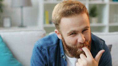 Evde oturma odasında kanepede oturan ve çok mutlu hissediyorum bir sürü donut yemek sakallı adam portresi.