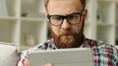 Evde oturma odasında kanepede oturan ve arkadaşlarınızla sohbet smartphone ile sakallı adam. Yakın çekim.