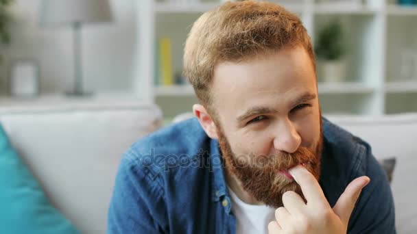 Porträtt av man med skägg äta en massa munkar samtidigt sitter på soffan hemma i vardagsrummet och känsla så glad. — Stockvideo